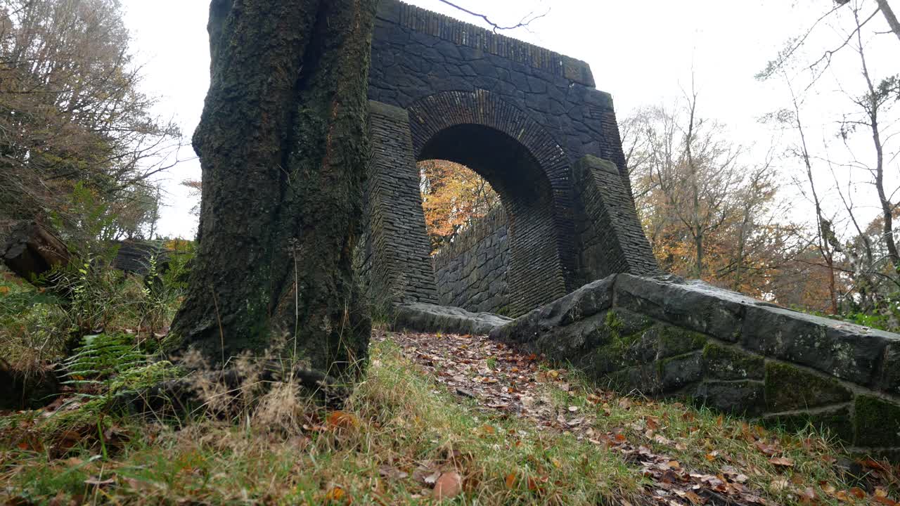 Ingresso a scala ad arco in pietra coperto di muschio verso rovine boschive su un fianco di collina autunnale nei giardini a terrazze di Rivington, dolly a destra.