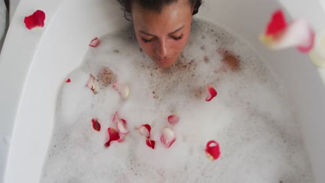 rose petals falling over african american woman relaxing in the bath tub in the bathroom at home