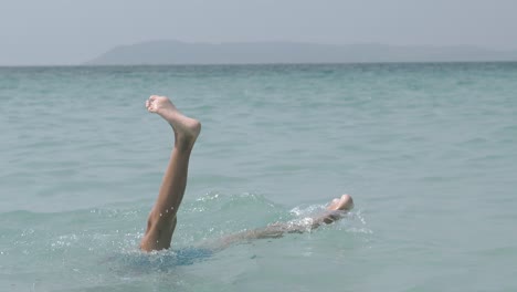 blonde boy in swimming trunks dives into water upside down