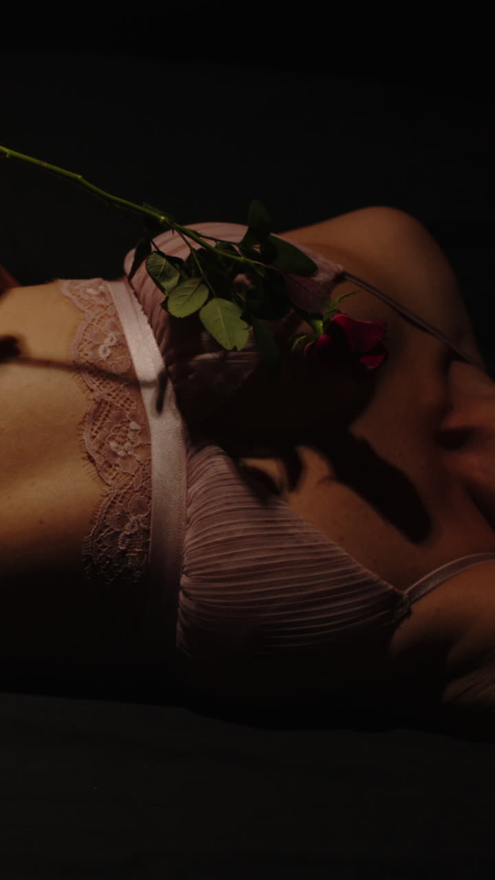 Stunning vertical of an attractive woman wearing enticing lingerie caressing her body with a rose