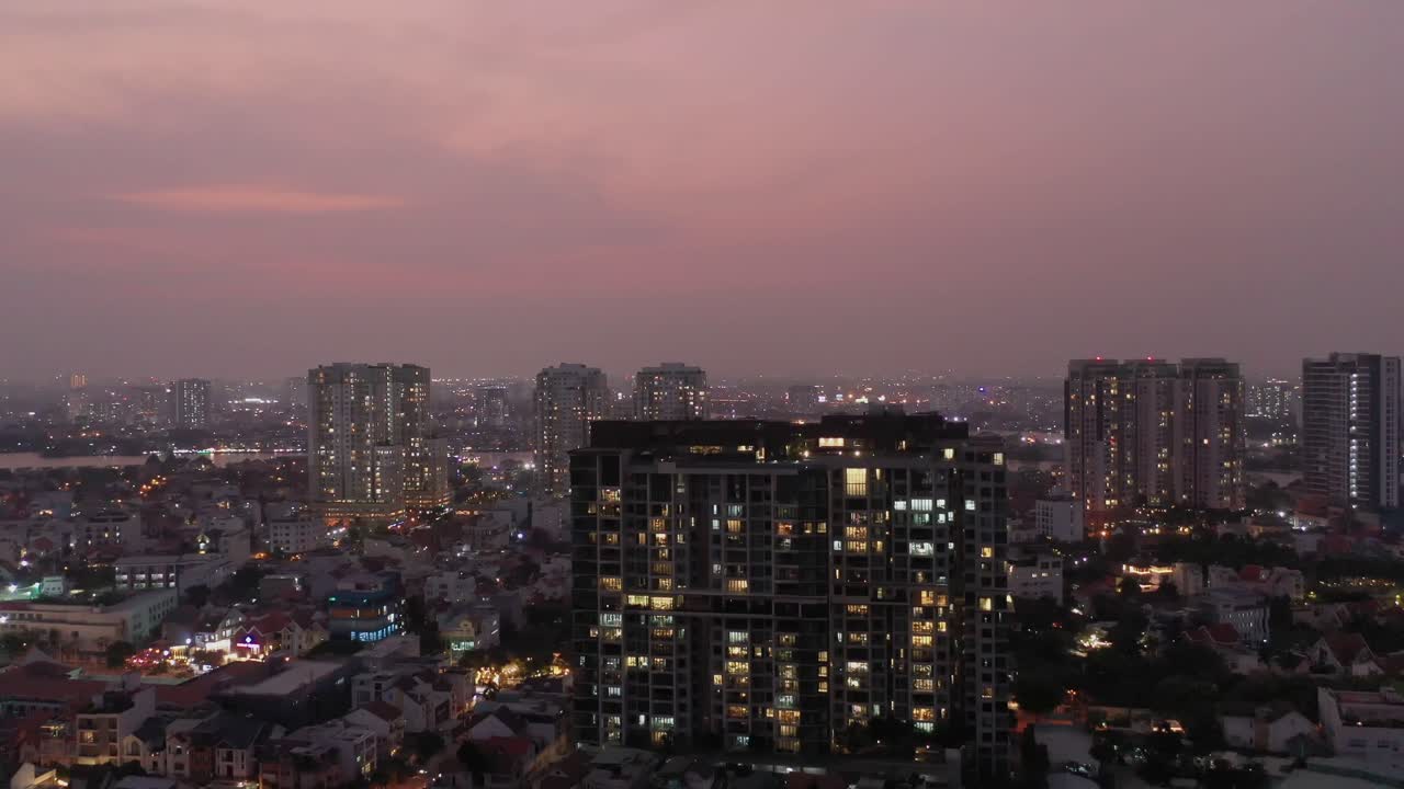 멀리 강이 있는 형형색색의 하늘을 배경으로 도시의 불빛, 건물, 집들이 있는 도시의 황혼 하강 드론