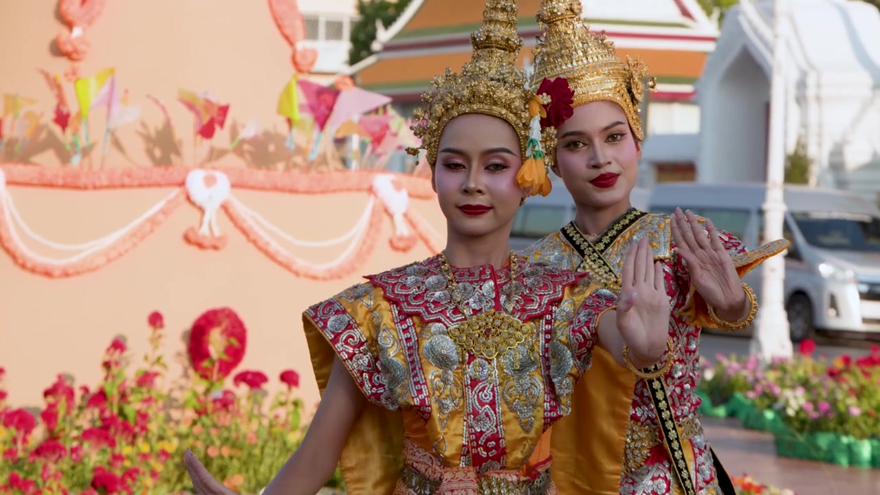 Dua seniman wanita menampilkan tari tradisional Thailand di luar ruangan mengenakan hiasan kepala emas yang rumit dan kostum merah