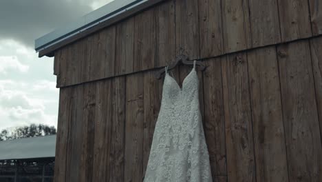 panning shot of a beautiful wedding dress hanging on the wall of a wooden shed