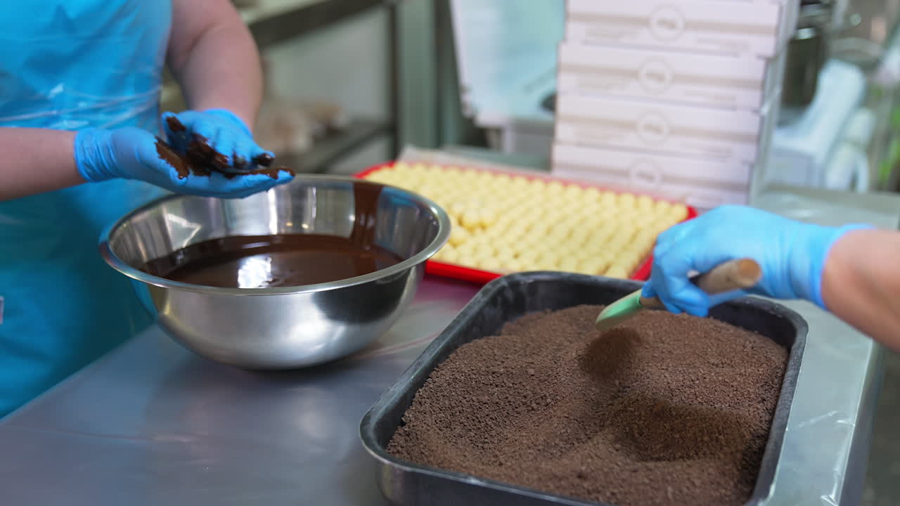 Female worker in latex gloves covers creamy candies with chocolate. Other worker coats chocolate balls with cocoa sprinkling. Candy making concept.