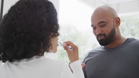 feliz pareja biracial cepillándose los dientes en un baño soleado, cámara lenta