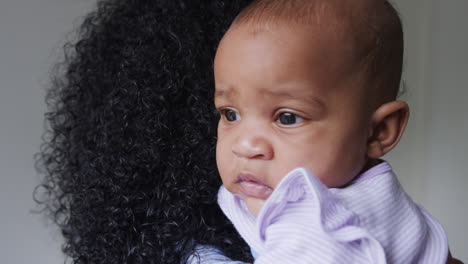 loving african american mother wearing pyjamas cuddling baby daughter in bedroom at home
