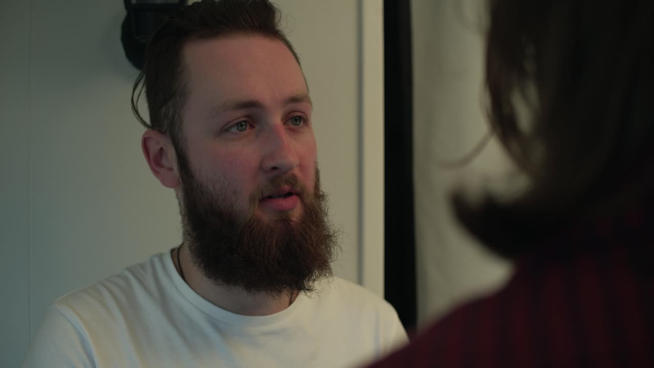 Een bebaarde man kijkt zachtjes naar een andere figuur, hun interactie gevuld met warmte en begrip. Een troostende hand op zijn schouder duidt op verbinding, geruststelling en steun