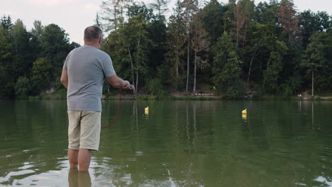 a man standing in a lake, throwing a rope with a magnet into the water