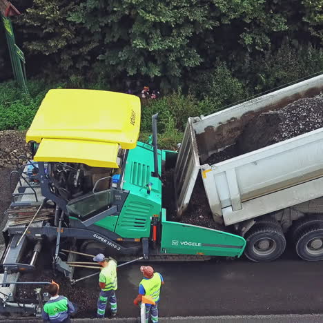 a process of laying asphalt by repairmen using an asphalt paver, a vibro-roller and a truck on a highway between cities. aerial view.