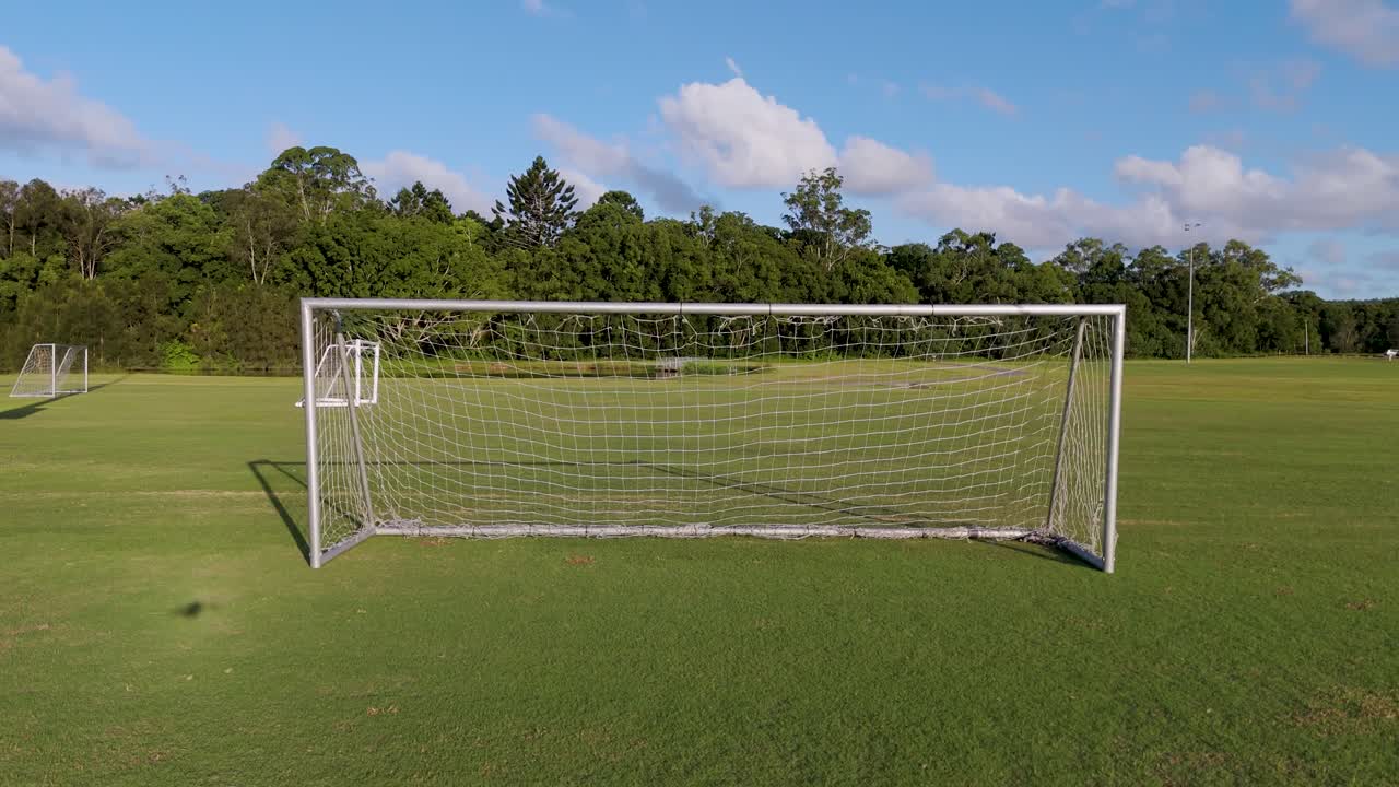 Aerial footage captures a soccer field with a goal, showcasing lush greenery and clear skies in a serene setting