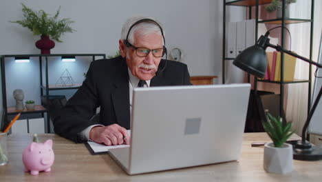 senior businessman in headphones making conference video call on laptop, call center agent, operator