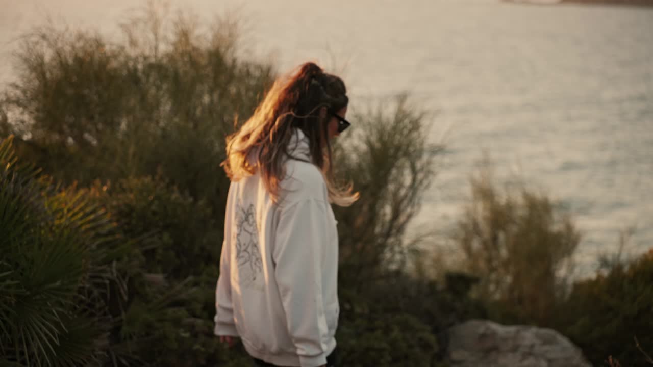 Young girl walking determinedly in slow motion along a cliff with the sea in the background