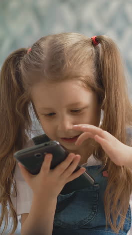 little children of different ages, show each other tongue, girl with pigtails holds smartphone, boy is blond - bottle with dummy, they sit on floor in living room, brother and sister smiling close up
