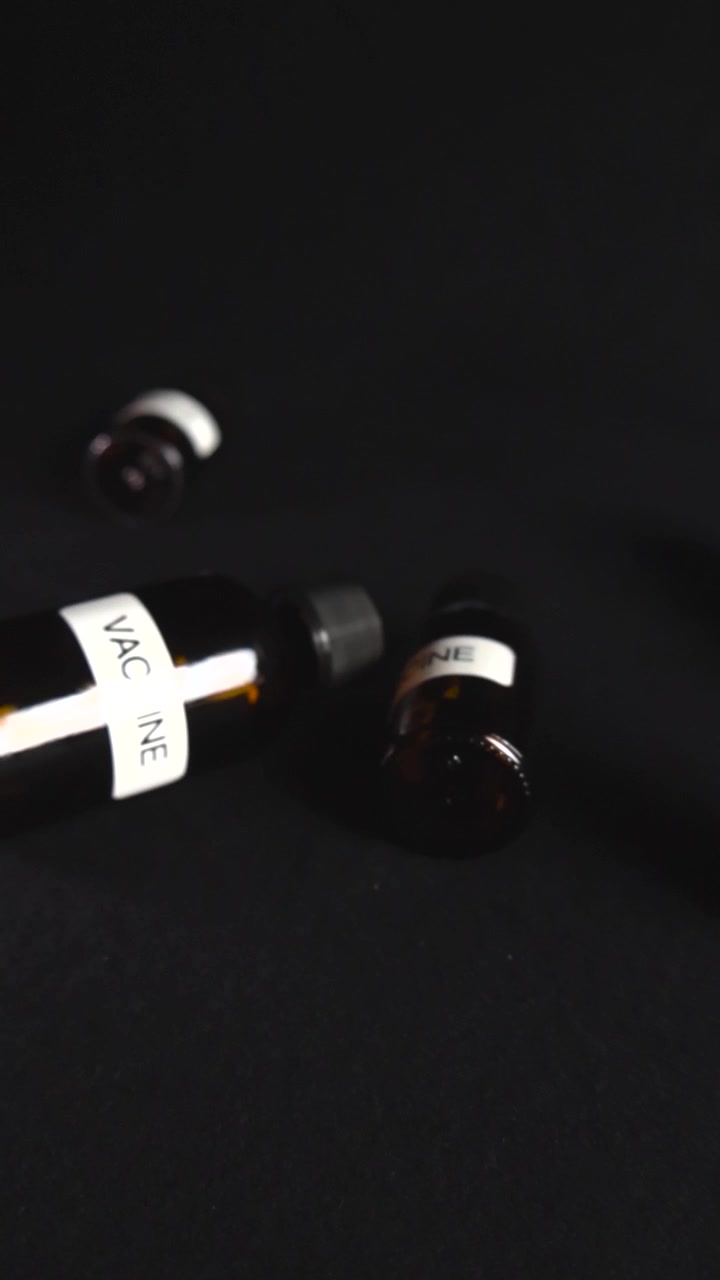 Numerose bottiglie di vetro scuro con etichette che recitano "vaccino" sparse su una superficie nera solida. Concetto medico che rappresenta la ricerca farmaceutica, lo sviluppo e la produzione di massa di nuovi farmaci.