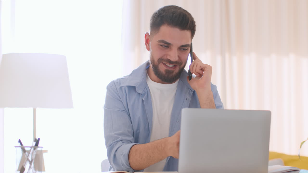 Young Man Working on Laptop and Talking on Smartphone