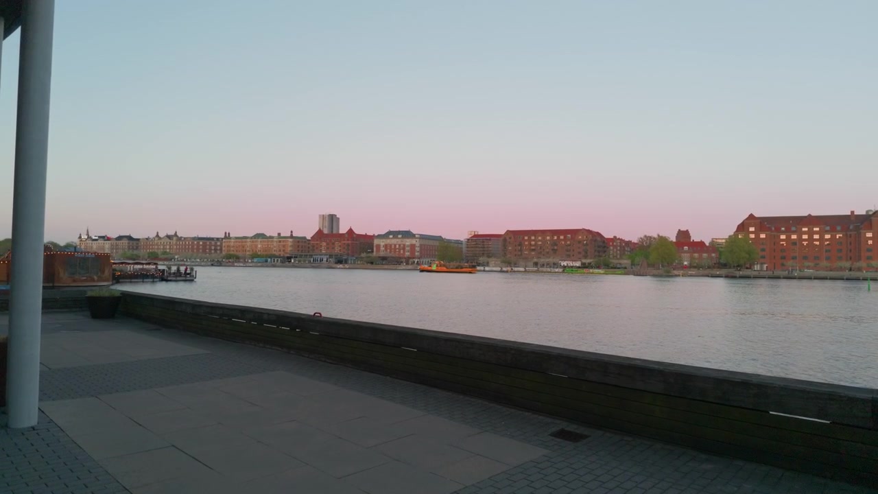 Byflod, solnedgang, bygninger, båd, gimbal stabilisatoroptagelse. 60fps filmisk indzoomning, mens man går fremad langs Københavns havnefront, der afslører et gult skib i Danmark.