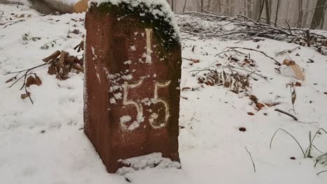 Close-up-view-of-stone-path-marker-in-snow-covered-forest-in-Germany,-Europe