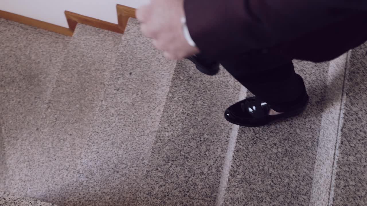 Close up of a man's polished black dress shoes stepping onto a staircase, wearing formal trousers
