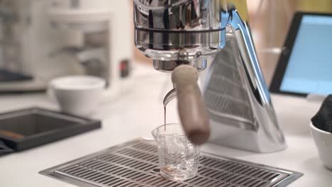 Handheld-frontal-view-of-espresso-dripping-out-of-coffee-machine-at-cafe-counter