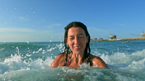 beautiful active woman having fun splashing with big sea waves breaking on his head