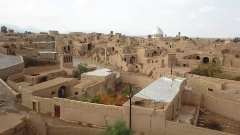 Pueblo-De-Ladrillos-De-Barro-En-El-Centro-De-La-Ciudad-Zona-Rural-Edificios-De-Casas-De-Adobe-Mezquita-Y-Ruinas-De-Civilización-Antigua-Gente-Local-Vida-En-El-Desierto-Amplia-Vista-Del-Horizonte-Cielo-Nublado-Sol-De-Verano-En-Arabia-Saudita-Yazd-Irán