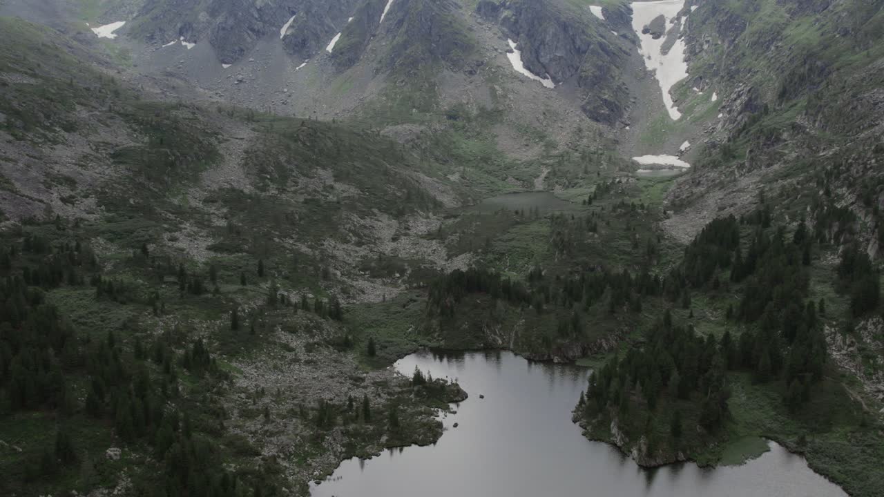 Filmato drone dei Laghi Karakol circondati da foresta di taiga e pendii rocciosi nella Repubblica dell'Altai, Russia, con chiazze di neve sulle creste montuose