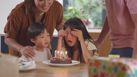 asian family celebrating birthday at home blowing out candles on cake