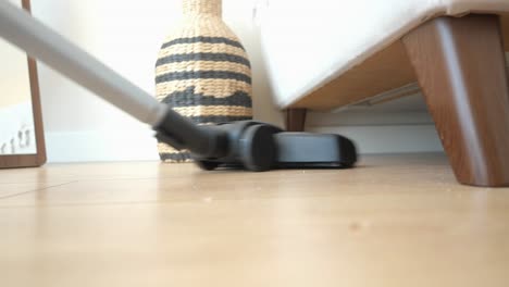 a vacuum cleaner cleaning a wooden floor under a couch