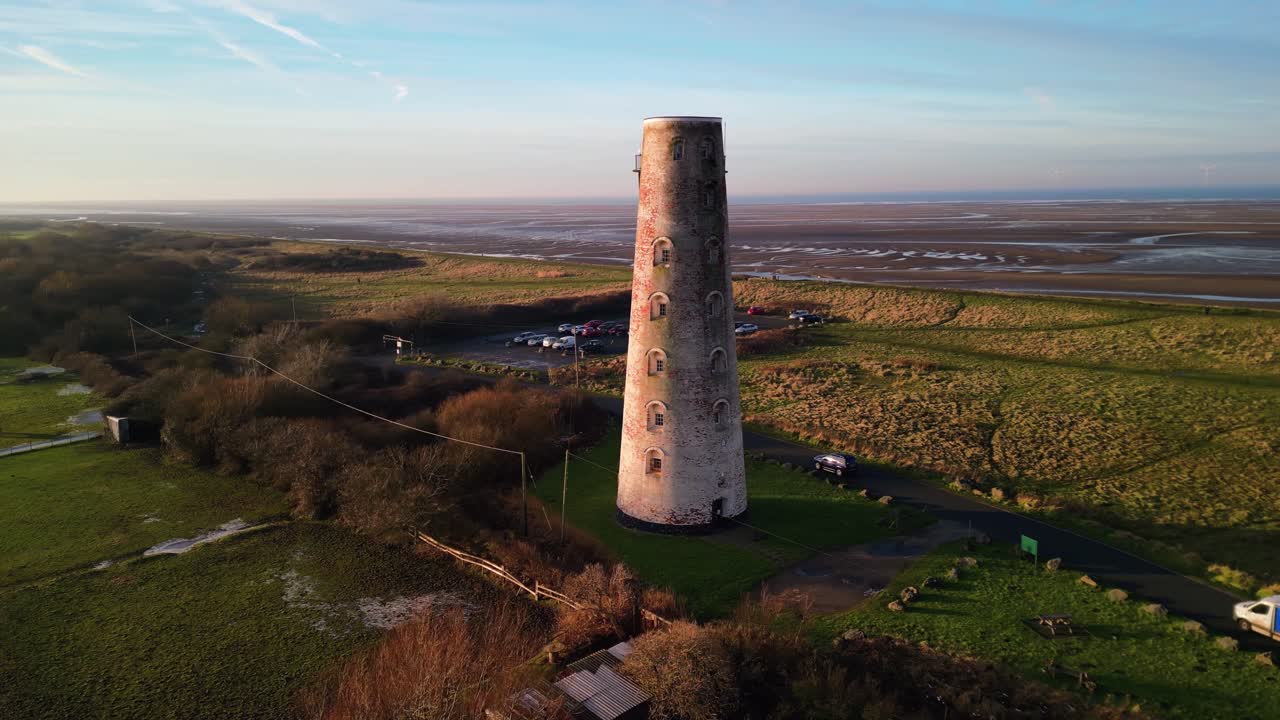 Beautiful aerial drone slow clockwise pan of Leasowe Lighthouse, revealing scenery at sunset in winter, UK