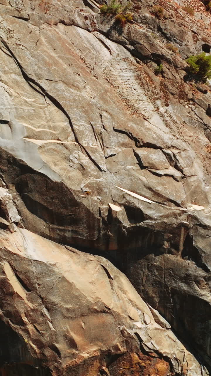 Close look at the bare grey rocks on sunny day. Huge cliff with rare greenery growing on the cliffs from top view. Vertical video