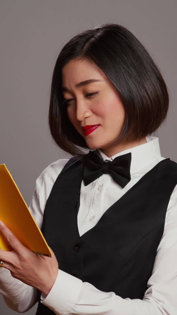Video verticale di una receptionist asiatica che legge un libro di letteratura su sfondo grigio