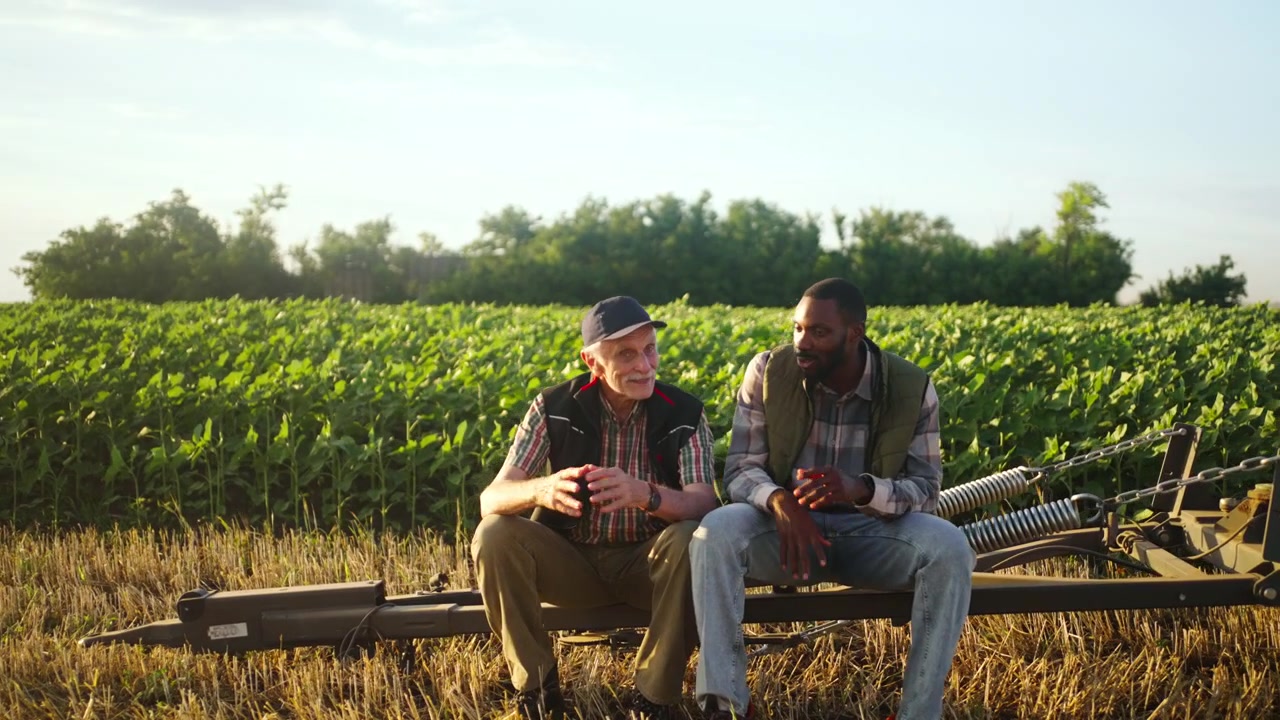 Two Farmers Talking While Sitting on Agricultural Equipment in a Field