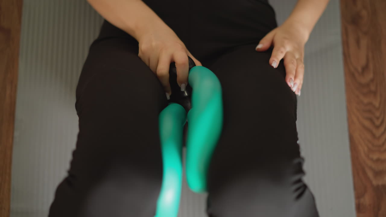 Woman exercises with thigh toning device closeup. Fitness enthusiast uses leg muscle trainer sitting on floor in personal fitness area. Improving body