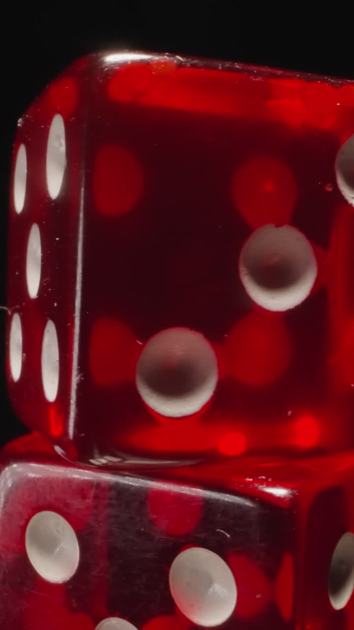 Stack of transparent red dices with certain number of white dots rotates on black background. Small cubes with spots designed for playing games macro