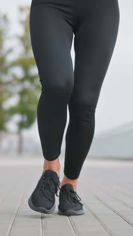 close-up of woman s legs in black leggings and sneakers jogging in outdoor path with blurred background of trees, poles, and iron fence, showcasing fitness and active lifestyle