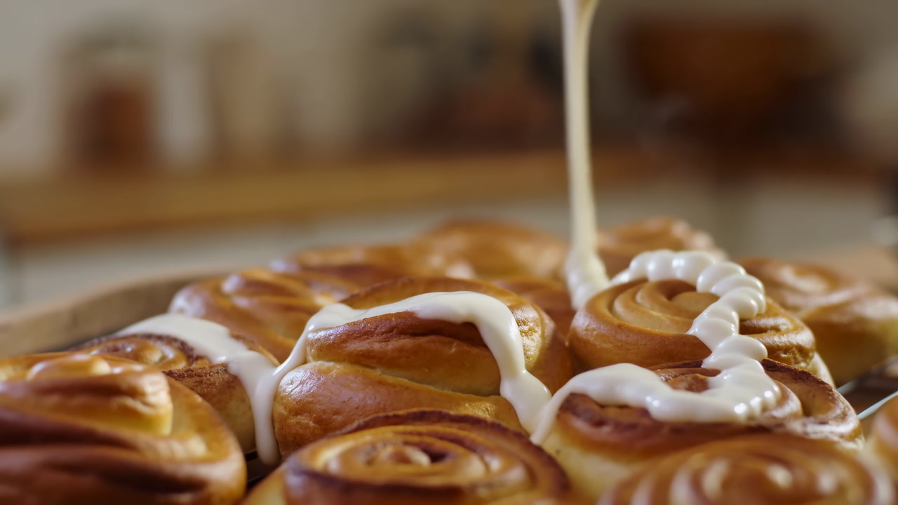 Fresh Cinnamon Rolls Being Drizzled With Glaze, Slow Motion Closeup Capturing Glossy Swirl And Creamy Icing