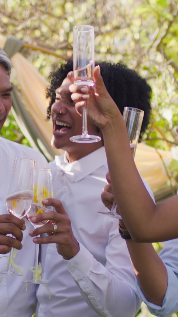 Vertical video: Lifting flute, center man in shirt bow tie with yellow rose pin toasting at wedding