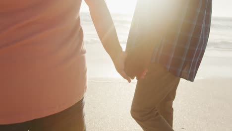 Senior-african-american-couple-holding-hands-and-walking-on-sunny-beach