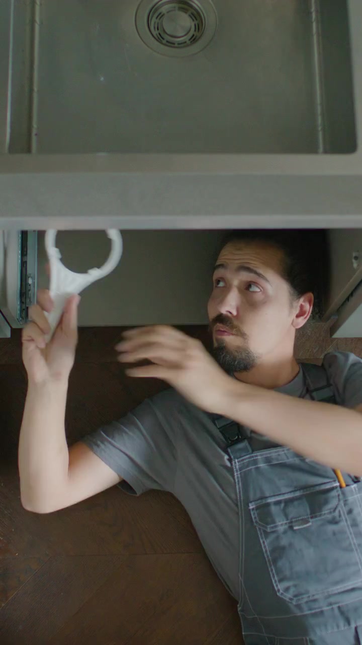 High Angle of Professional Plumber in Overalls Repairing Leaky Kitchen Sink