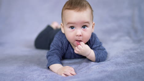 adorable caucasian child lies on belly with his finger in mouth. lovely sweet baby resting peacefully on the grey plaid. close up. blurred backdrop.