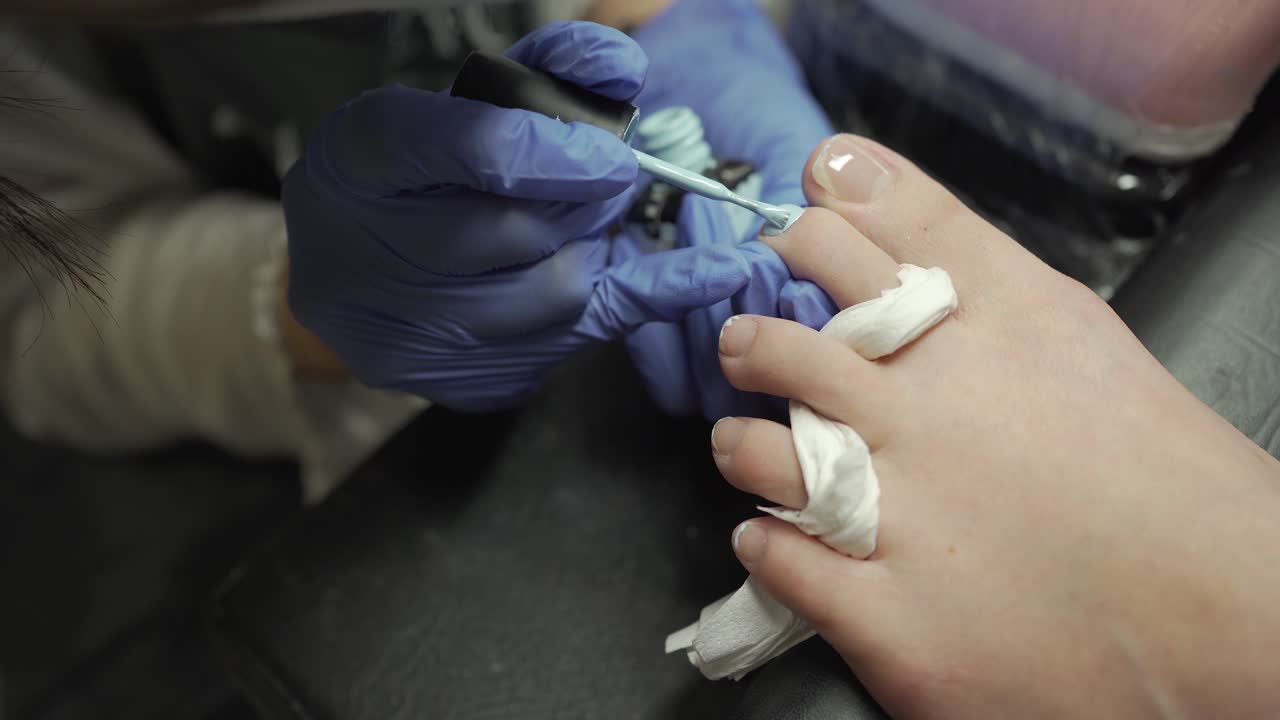 manicurist applying baby blue color nail polish on customer's toenails