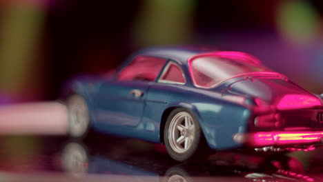 blue die-cast model car bathed in vibrant pink light