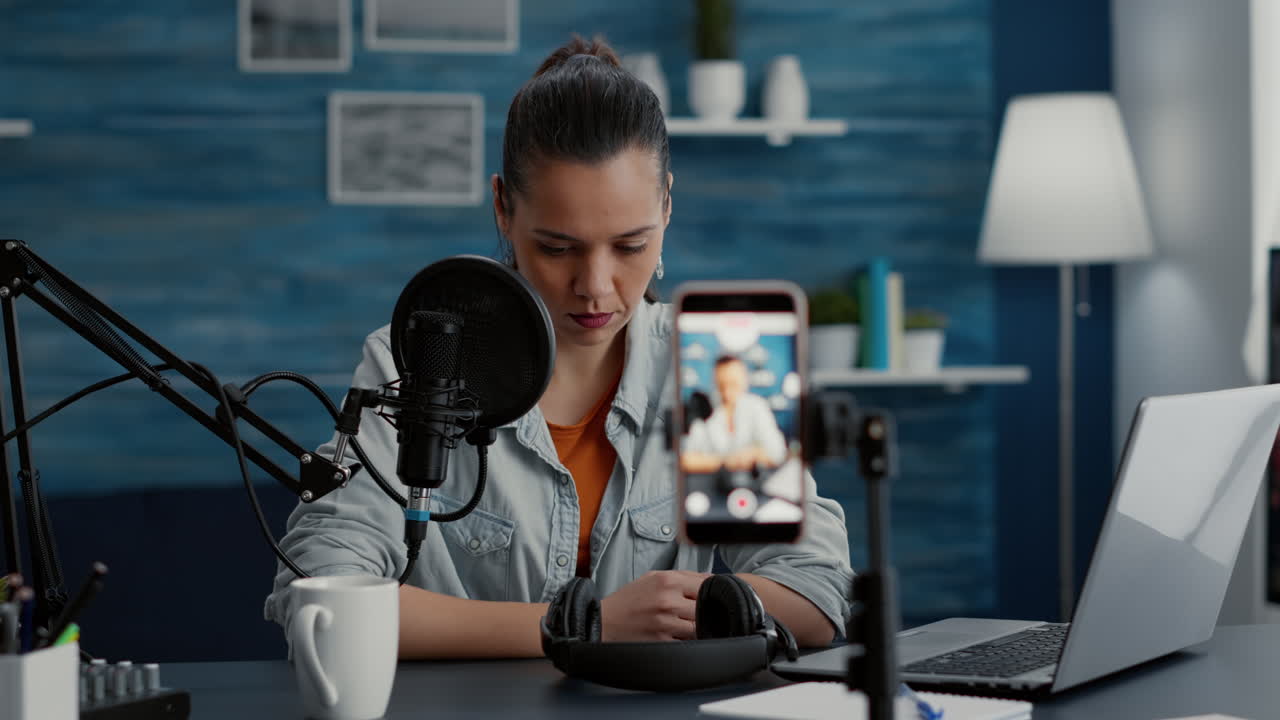 Creatore di contenuti digitali creativi seduto alla scrivania del suo studio domestico mentre filma un vlog con lo smartphone