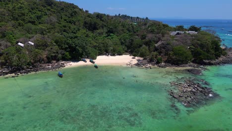 Luftaufnahme-Eines-Tropischen-Inselstrandes-Mit-Türkisfarbenem-Wasser,-Auf-Dem-Longtail-Boote-Warten,-Die-In-Thailand-Auf-Touristen-Warten