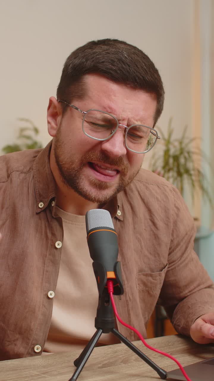 Giovane cantante blogger caucasico positivo che usa il portatile mentre canta nel microfono al tavolo