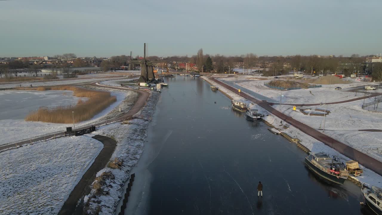 Luftfoto af Strijkmolen vindmølle og skøjteløbere på frossen flod ved solopgang i Alkmaar, Holland, med fantastisk solopgangsbelysning, rolig atmosfære, droneoptagelser i høj kvalitet der afslører fredfyldt landskab.