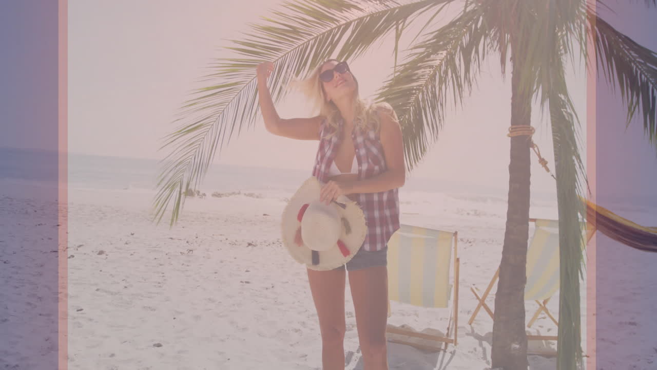 Wearing sunglasses and holding hat, woman relaxing under palm tree on beach