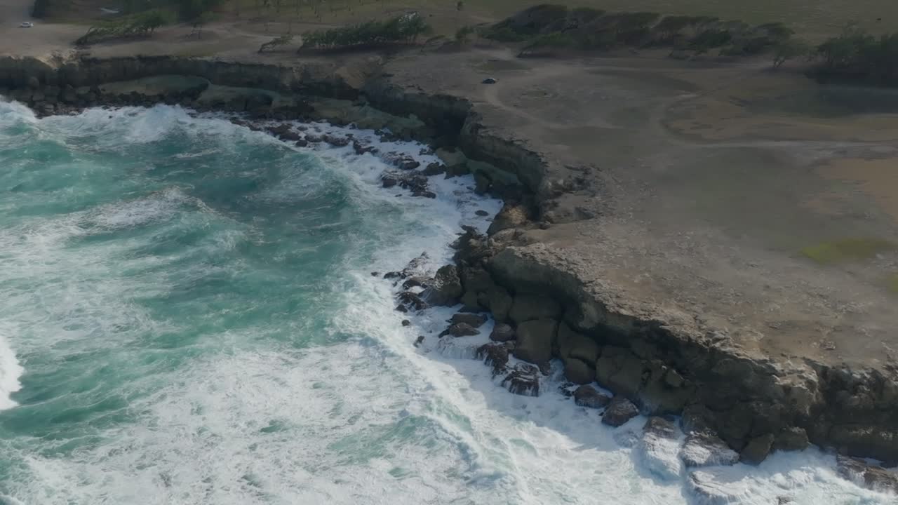Oceanic waves roll in crashing spreading white wash and spray on crumbling coastal sea cliff