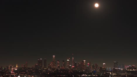aerial telephoto dolly shot of a full moon over the downtown skyline at night in los angeles, california. 4k
