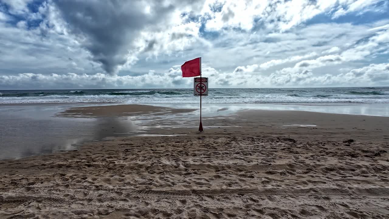 красный флаг, запрещающий плавать, дул в ветру на пляже русалки, предупреждая о опасном течении.